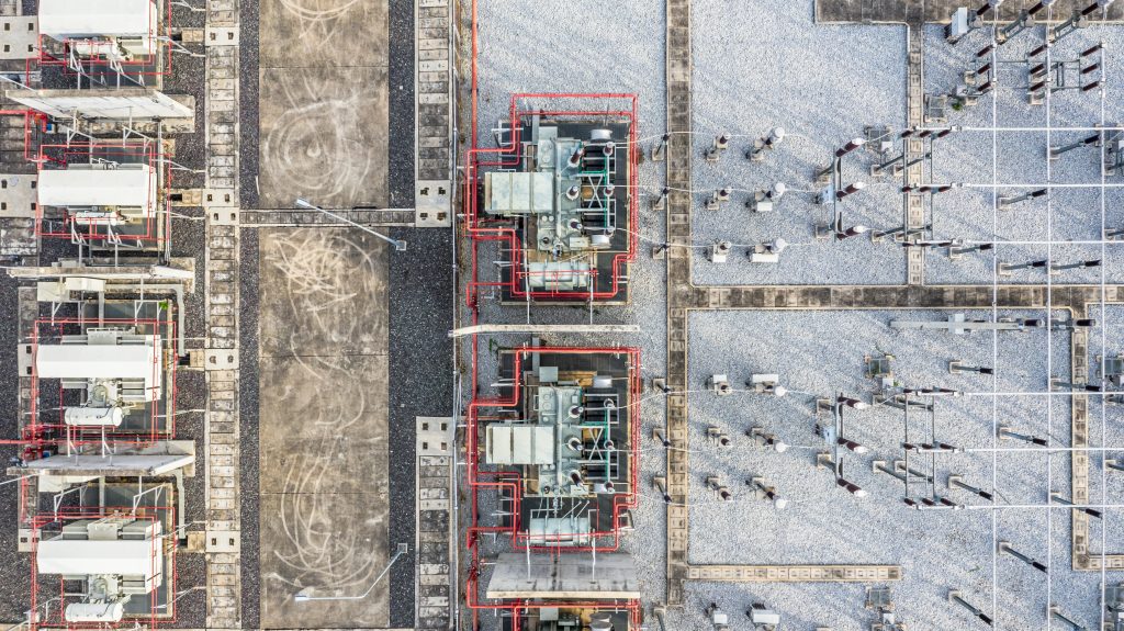 Aerial view from a drone looking straight down at high-voltage power transmission infrastructure, some sort of substation or transformer assembly, and a part of the power grid.