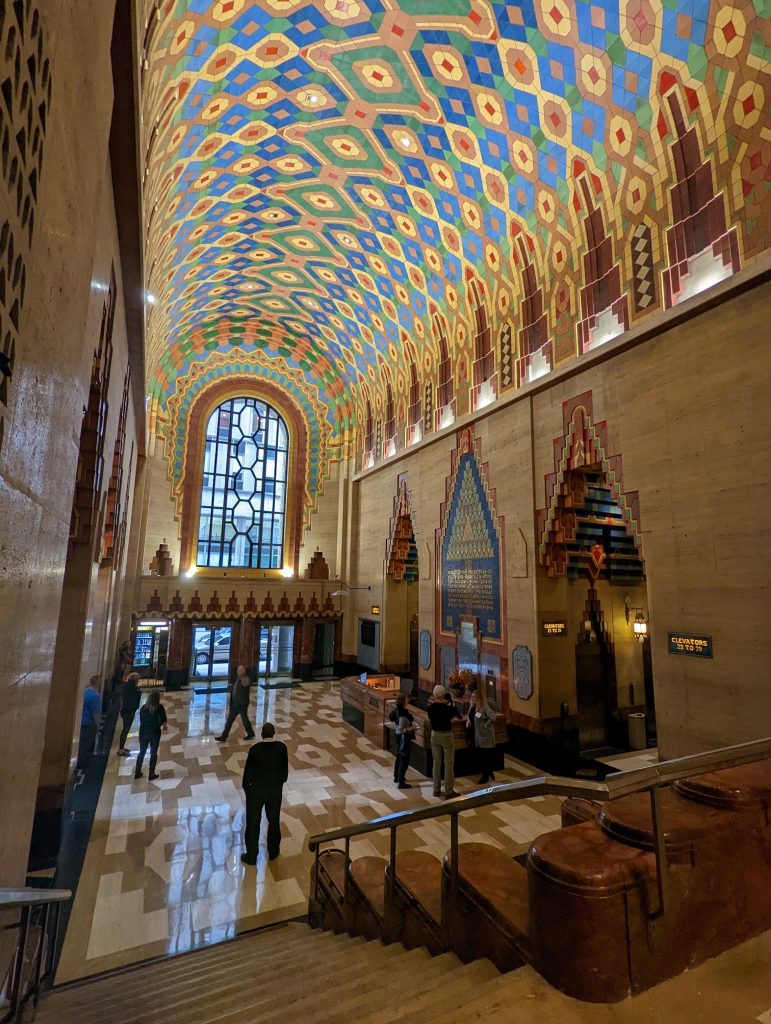 A wide angle shot of the lobby of the Guardian Building in downtown Detroit, with its vibrant, tiled ceiling and elegantly mullioned window featured prominently.